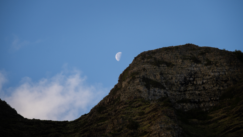 The moon in a blue sky, above a small mountain